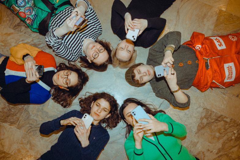 Students are lying on the floor with their phones in their hands.